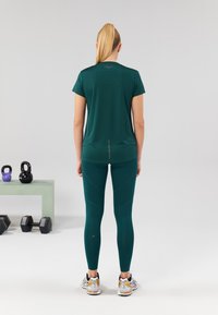 Teal athletic t-shirt with short sleeves and a reflective seam detail, paired with teal leggings featuring angled seam patterns and running shoes.