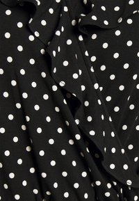 Svart tyg med jämnt fördelade vita prickar och ett rynkat sömdetalj.