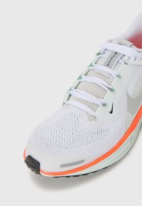 Baskets blanches avec une tige en mesh, des détails texturés, un swoosh en argent signature et des accents orange vif sur la semelle.