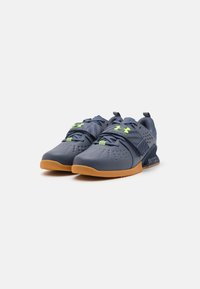 Blue athletic shoes with perforated upper, green accent details, and a gum rubber outsole. Features a secure strap and padded collar.