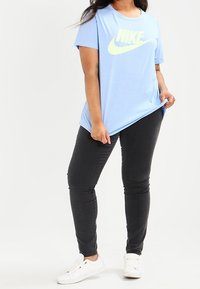 Ljusblå Nike t-shirt med kort ärm och stor gul logotyp, kombinerad med svarta slim-fit byxor och vita sneakers.