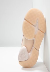 Podeszwa buta z jasnobeżowego materiału gumowego, z teksturowanym wzorem zapewniającym przyczepność oraz gładką, zaokrągloną częścią pięty.