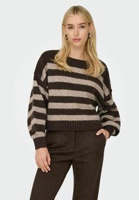 Pull rayé marron et beige avec un col rond, coupe loose, et des poignets et un ourlet côtelés, associé à un pantalon marron foncé.