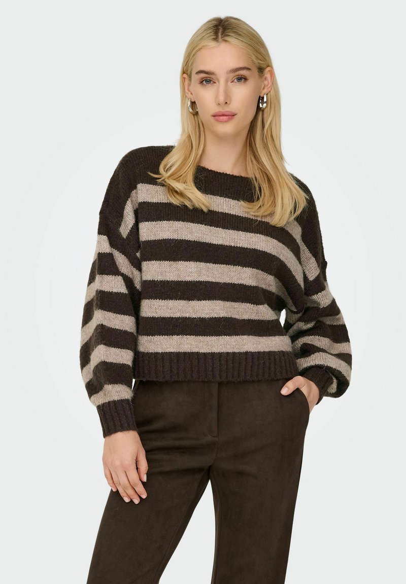Pull rayé marron et beige avec un col rond, coupe loose, et des poignets et un ourlet côtelés, associé à un pantalon marron foncé.