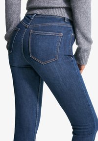 Tanke modre kavbojke z gladko teksturo, z zadnjimi žepi in kontrastnim šivanjem. Pas je visok in prilagojen.