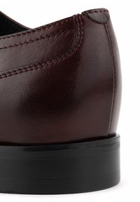Burgundzkie skórzane buty o gładkim wykończeniu, czarna gumowa podeszwa, staranne przeszycia wzdłuż szwu i zaokrąglony design obcasa.