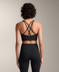 Reggiseno sportivo nero con spalline incrociate, fascia alta e design senza cuciture, abbinato a leggings neri a vita alta con una texture liscia.