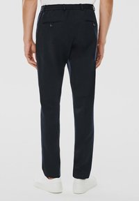 Granatowe spodnie wykonane z tkaniny o splocie, z elastycznym pasem, posiadające dwie tylne kieszenie z zapięciem na guziki oraz dopasowany krój.