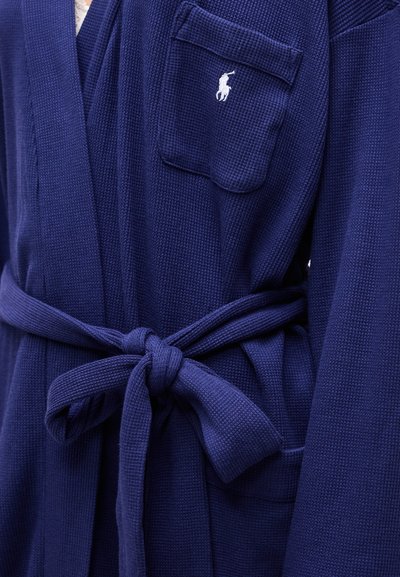 Σκούρο μπλε ρόμπα με υφή βάφλας, ζώνη δεμένη στη μέση και τσέπη στο στήθος με λευκό κεντημένο λογότυπο παίκτη πόλο.