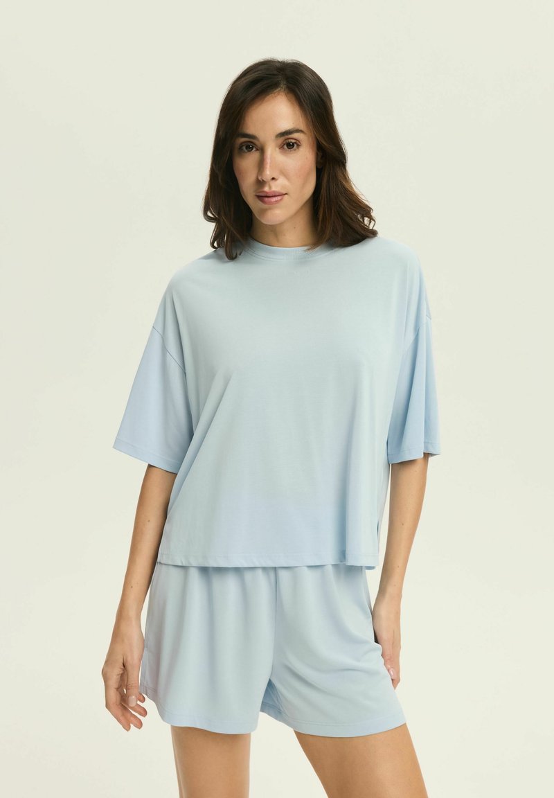 Jasnoniebieski zestaw odzieży domowej składający się z luźno dopasowanej bluzki z krótkim rękawem i pasujących szortów. Miękka tkanina o gładkiej strukturze.