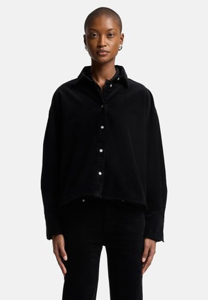 Camicia in corduroy nera con colletto a camicia, maniche lunghe e vestibilità rilassata. Presenta bottoni bianchi e un tessuto testurizzato.