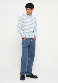 Langärmliges Polohemd in Hellblau mit weißen und grauen Streifen, kombiniert mit lockeren blauen Jeans und schwarzen klobigen Schuhen.