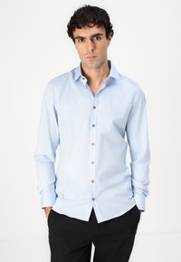 Lichtblauw overhemd met lange mouwen en een button-down kraag, voorzien van brown knopen en een subtiele textuur, gecombineerd met zwarte broeken.