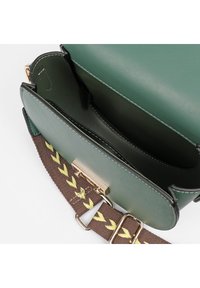 Borsa a mano in pelle verde con texture liscia, tracolla marrone con motivo a zigzag giallo e chiusura e dettagli in metallo dorato.