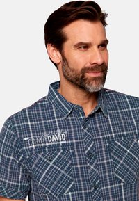 Camicia a maniche corte a quadri in blu e bianco. Presenta un colletto a bottoni, due tasche sul petto e un logo stampato sul lato sinistro.
