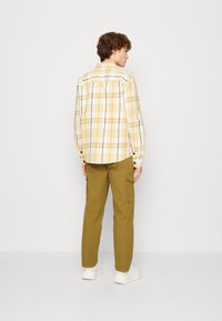 Chemise à carreaux jaune et blanche avec des accents noirs, associée à un pantalon cargo vert olive et des sneakers blanches. Vue de l'arrière.