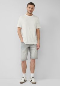 T-shirt bianca a maniche corte con scollatura rotonda, abbinata a pantaloni corti in denim grigio chiaro. Indossata con sneakers bianche e beige e calzini alla caviglia.