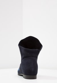 Botín de ante azul marino con textura suave, parte superior redondeada y suela plana negra. Presenta un detalle de costura decorativa en el lateral.