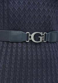 Ζώνη σε σκούρο μπλε χρώμα, κατασκευασμένη από ύφασμα με υφή, που διαθέτει ασημένια αγκράφα σε σχήμα G και λεία δερμάτινη λωρίδα στο πλάι.