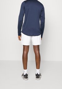 Mekko navy pitkähihainen urheilupaita valkoisten shortsien kanssa; henkilöllä on mustat ja harmaat lenkkarit sekä valkoiset sukat. Sileä, hengittävä kangas.
