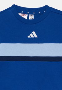 Μπλε φούτερ με ανοιχτό μπλε οριζόντιο ρίγες και μπλε σκούρα ταινία. Λευκό λογότυπο Adidas στην αριστερή πάνω πλευρά. Πλεκτή υφή.