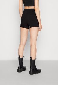 Pantalones cortos de mezclilla negra con cintura alta y dos bolsillos traseros, combinados con botines negros. El material parece suave con un diseño ajustado.