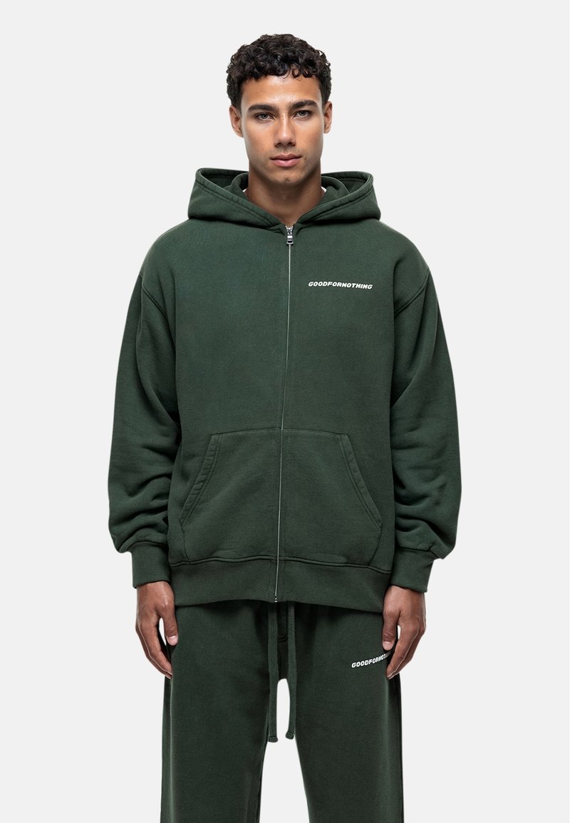 Felpa verde con zip realizzata in tessuto morbido, dotata di tasche a kangaroo. Presenta una stampa del logo frontale e un cappuccio con coulisse. Vestibilità classica.