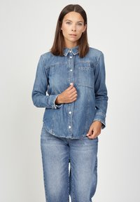 Denim shirt with a classic collar, front pocket, button closure, and long sleeves. Light blue color with subtle fading and frayed hem details.
