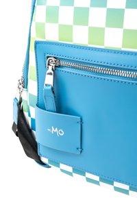 Mochila de cuadros con patrón verde y blanco, bolsillo con cremallera azul y una etiqueta de logo. Fabricada con material sintético duradero y textura suave.
