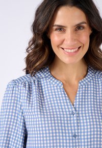 Blusa con colletto caratterizzata da una fantasia a quadri leggeri blu e bianchi, chiusura con bottoni e spalle arricciate con una morbida texture.