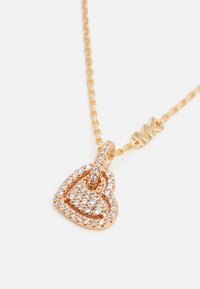 Collana in tono oro con un pendente a forma di cuore decorato con strass trasparenti. La catena presenta anelli dettagliati che si collegano al pendente.