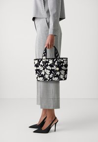 Černobílá kabelka s květinovým vzorem, se dvěma krátkými uchy, obdélníkového tvaru a s kulatým zlatým kováním.