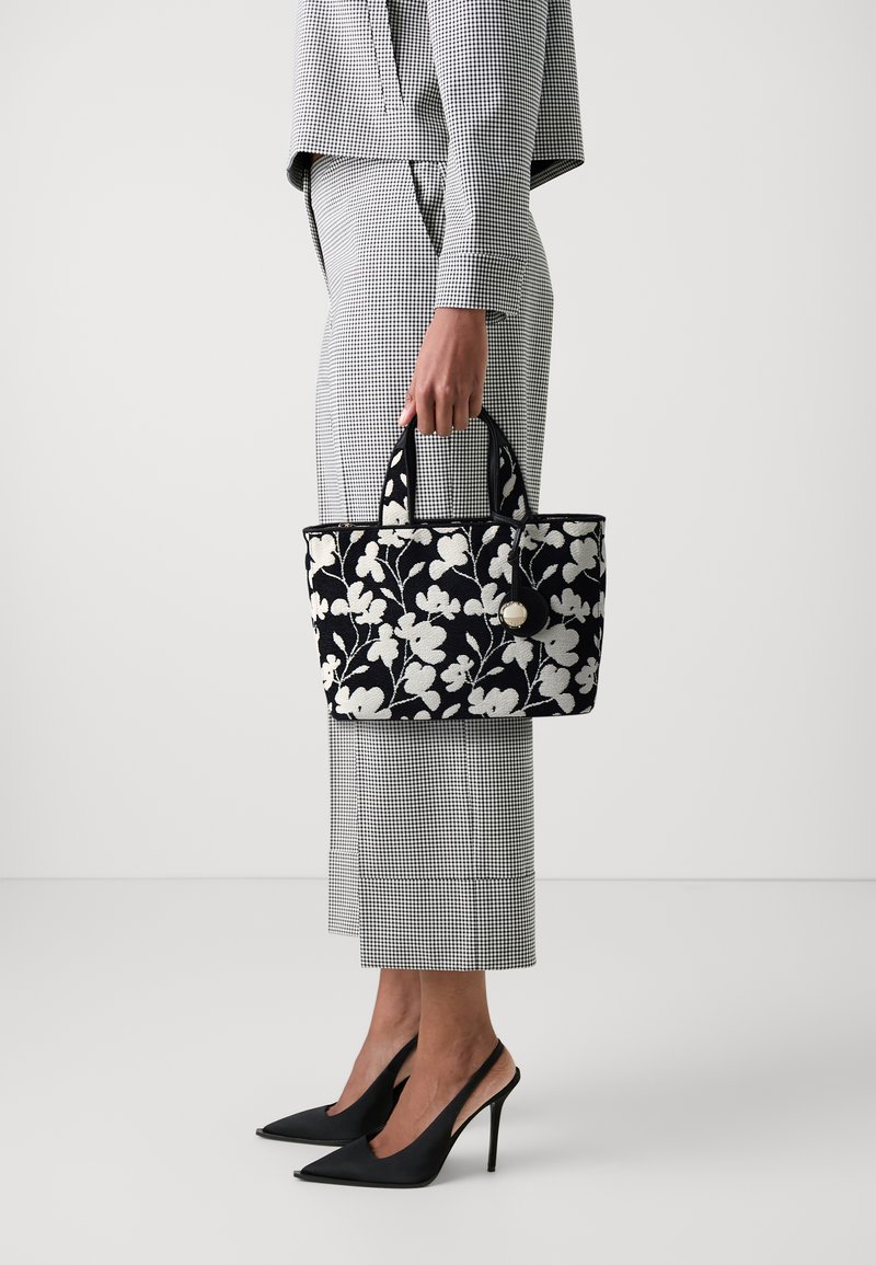 Černobílá kabelka s květinovým vzorem, se dvěma krátkými uchy, obdélníkového tvaru a s kulatým zlatým kováním.