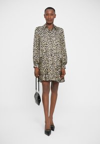 Vestido de camisa con estampado de leopardo en beige y negro, de mangas largas, con cuello abotonado y un dobladillo fluido. Combinado con tacones altos negros y un bolso pequeño.