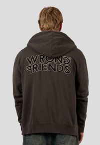 Tmavě šedá mikina s kapucí, na zadní straně s textem "WRONG FRIENDS" v kontrastní prošívané písmu. Měkký materiál, uvolněný střih.