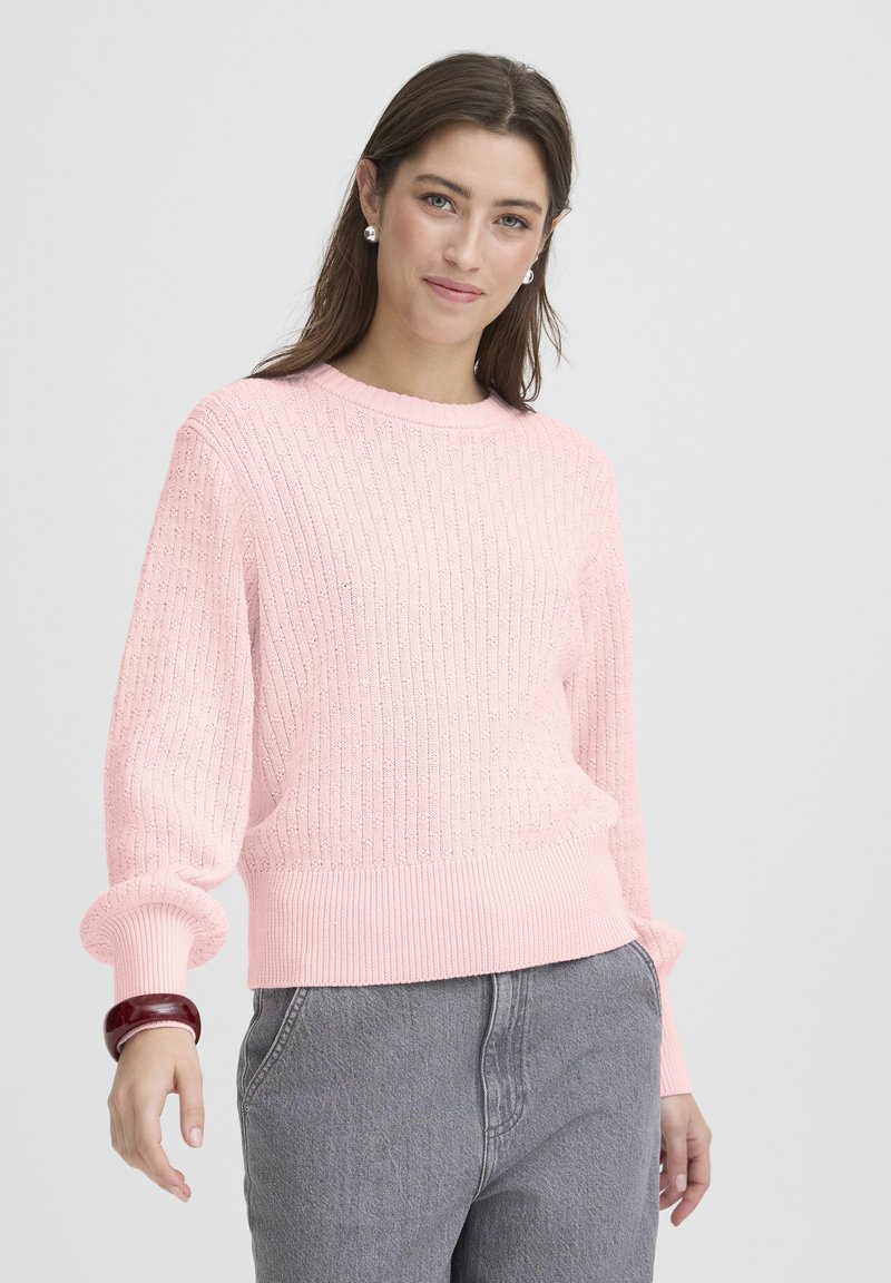 Pull rose avec texture côtelée, col rond et manches bouffantes. Associé à un jean gris taille haute, complété par un bracelet rond.