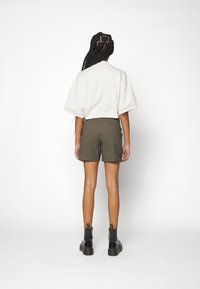 Weißes kurzärmliges Oberteil kombiniert mit olivgrünen Shorts. Das Model trägt schwarze Stiefel mit einem strukturierten Absatz. Einfaches, sauberes Design.