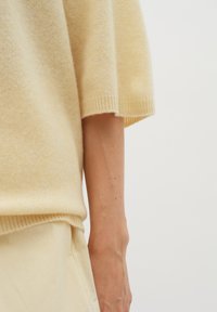 Grietos spalvos megztinis su laisvu siluetu, apvaliu iškirpimu ir trumpomis rankovėmis. Minkšta tekstūra su ribotais hemų akcentais.