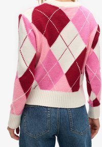Vista posteriore di una persona che indossa un maglione a maglia argyle rosa, rosso e bianco abbinato a jeans di denim blu.