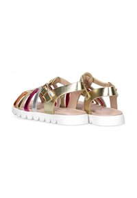 Sandalias metálicas doradas con tiras multicolores en plata, púrpura, naranja y rojo. Presentan una suela blanca gruesa y hebillas ajustables.