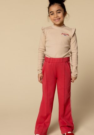 Beige langwerpige top met geruwde schouders en een rode "Amour" logo, gecombineerd met felrode sweatpants met zijstrepen en een elastische tailleband.