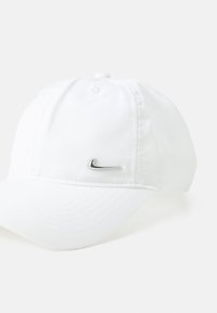 Λευκό καπέλο από ύφασμα, με καμπύλη γείσο, ραμμένες λεπτομέρειες και μεταλλικό ασημί λογότυπο Nike στο μπροστινό αριστερό μέρος.