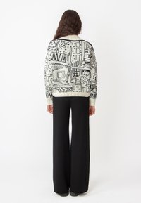 Gebreide trui in crème met zwarte abstracte ontwerpen; geribde halslijn en manchetten. Hoge taille, wijde zwarte broek. Gladde textuur.