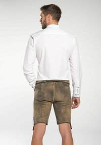 Witte lange mouwen shirt, gecombineerd met bruin leren shorts tot de knie met rode accenten en een textuur. Zichtbare knoopdetails.