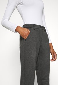 Grijze gestreepte broek van een textuurstof, met een knoopsluiting, riemlussen en zijzakken, gecombineerd met een wit langemouwen top.