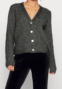 Objemný šedý kardigan s výstřihem do V, dlouhými rukávy a pěti velkými stříbrnými knoflíky. Texturovaná pletenina a zkrácený lem.