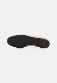 Semelle de chaussure plate avec un dessous en caoutchouc noir, présentant un dessus beige et un logo estampé. Texture lisse avec un design à bout rond.