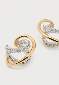 Σκουλαρίκια κρίκοι από χρυσό και ασημί, στριφογυριστά, με ενσωματωμένα καθαρά κρύσταλλα σε λευκό φόντο.