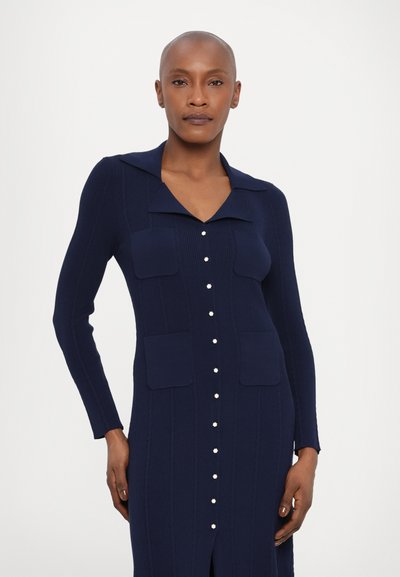 Abito in maglia blu navy con colletto, maniche lunghe e due tasche a toppa. Caratterizzato da chiusura con bottoni bianchi e design a coste testurizzato.