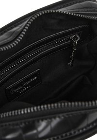 Schwarze Handtasche mit Innenraum, der eine Reißverschlusstasche, glattes Stofffutter und ein markiertes Etikett aufweist. Die Außenseite hat eine strukturierte Oberfläche mit tonal abgestimmten Nähten.